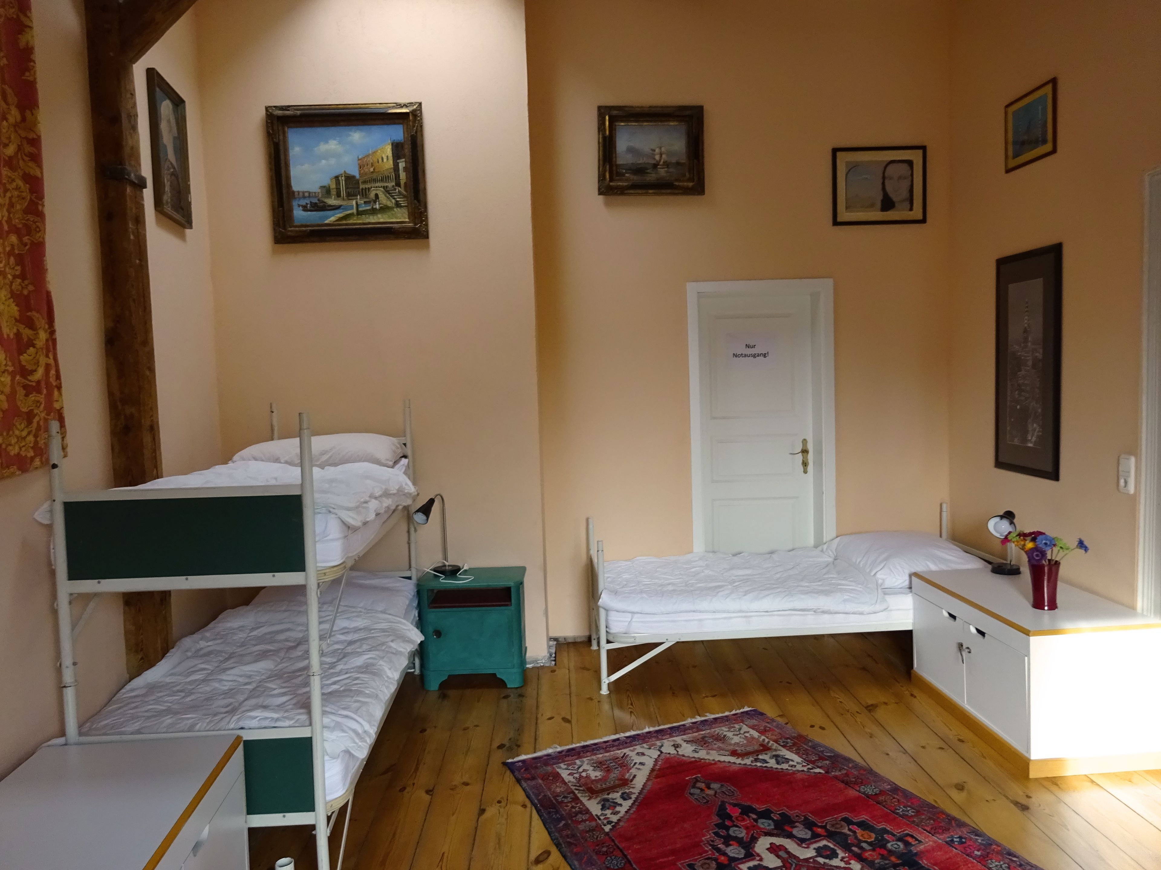 Ein Zimmer mit zwei Etagenbetten, einem Schreibtisch, einem Stuhl, einer Tür und mehreren gerahmten Bildern an den Wänden.