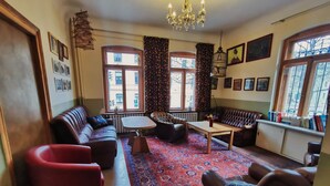A cozy living room with a red sofa, a brown leather armchair, a wooden coffee table, and a patterned rug. - Hummel Hostel (Weimar)
