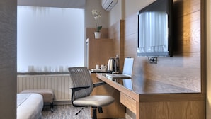 Una habitación de hotel con una cama, un escritorio con una computadora portátil, una silla, un televisor y una planta en maceta.