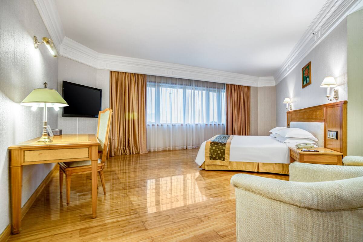 Una habitación de hotel con un escritorio de madera, una cama, una silla y un televisor.