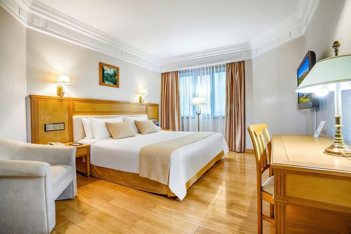 A hotel room with a large bed, a wooden headboard, a desk with a chair, and a television.