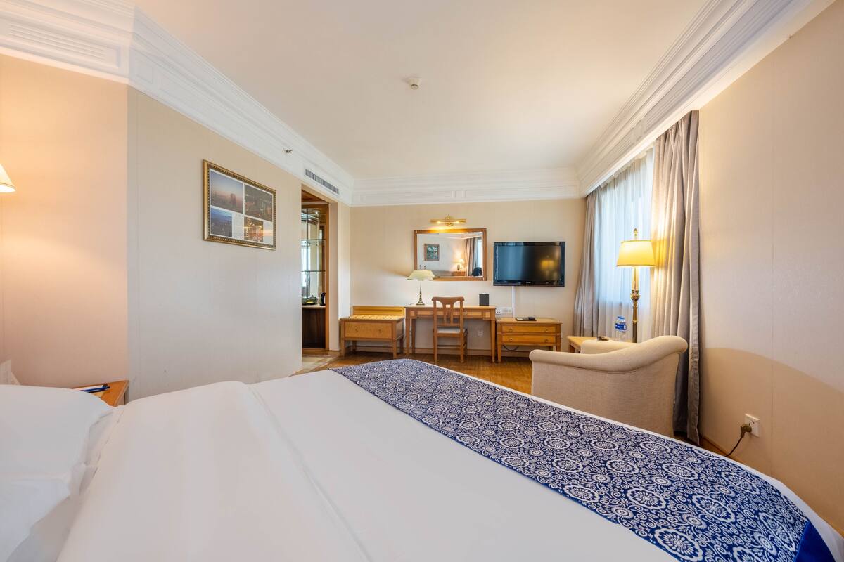 Una habitación de hotel con una cama grande, un escritorio con silla, un televisor y una ventana con cortinas.