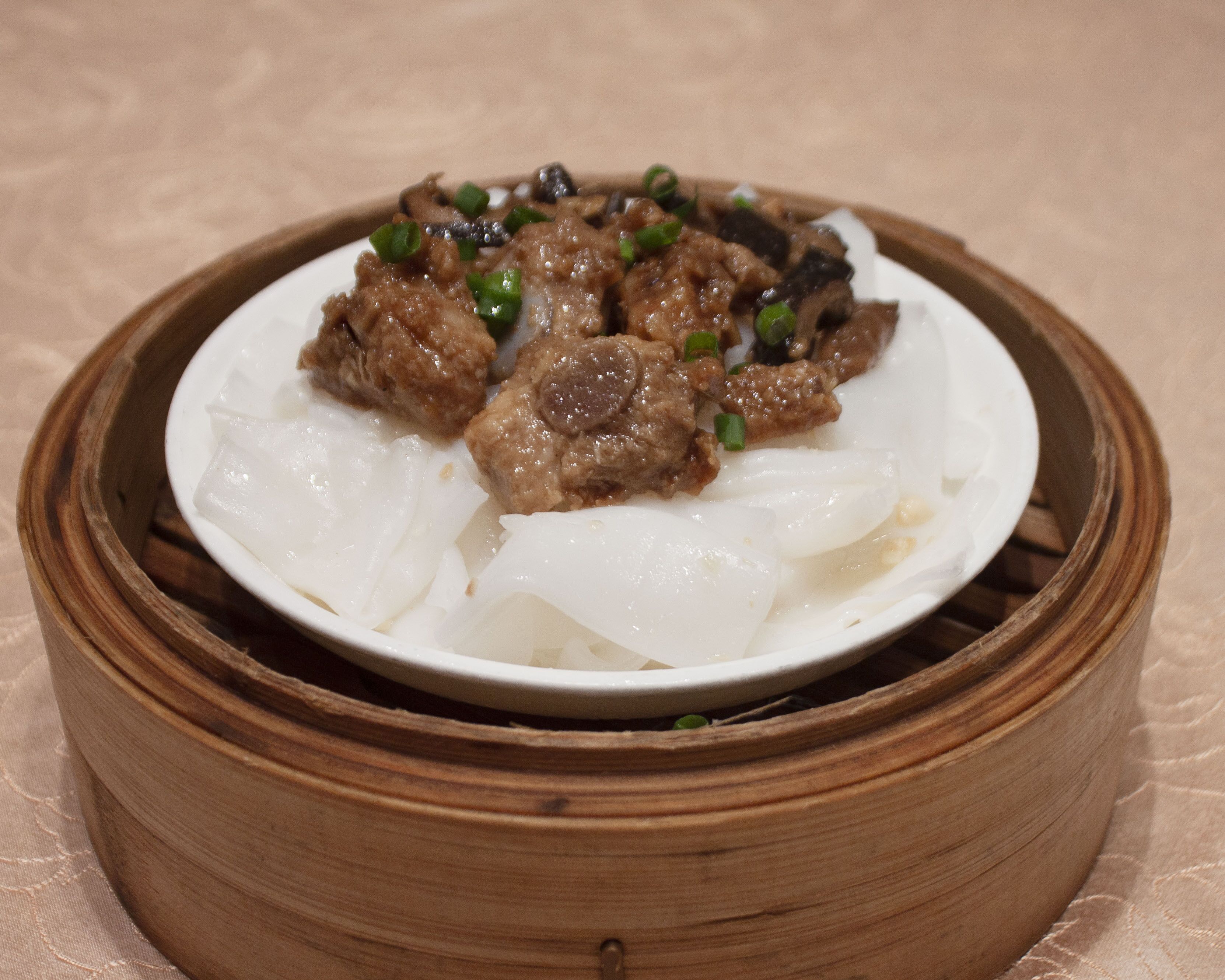 A plate of food with meat and vegetables on a white plate inside a bamboo steamer.
