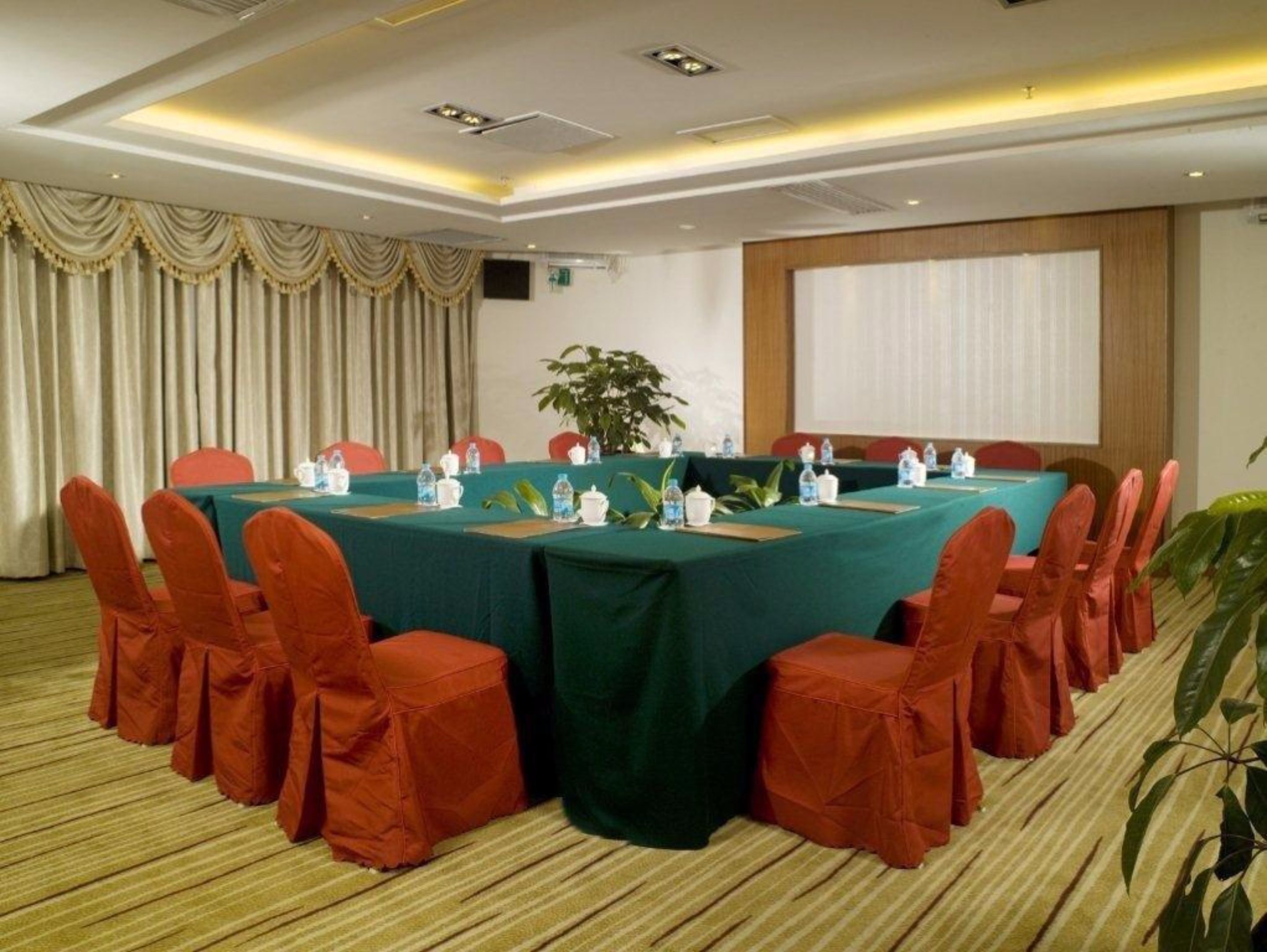 A conference room with a long table, red chairs, and a projector screen.