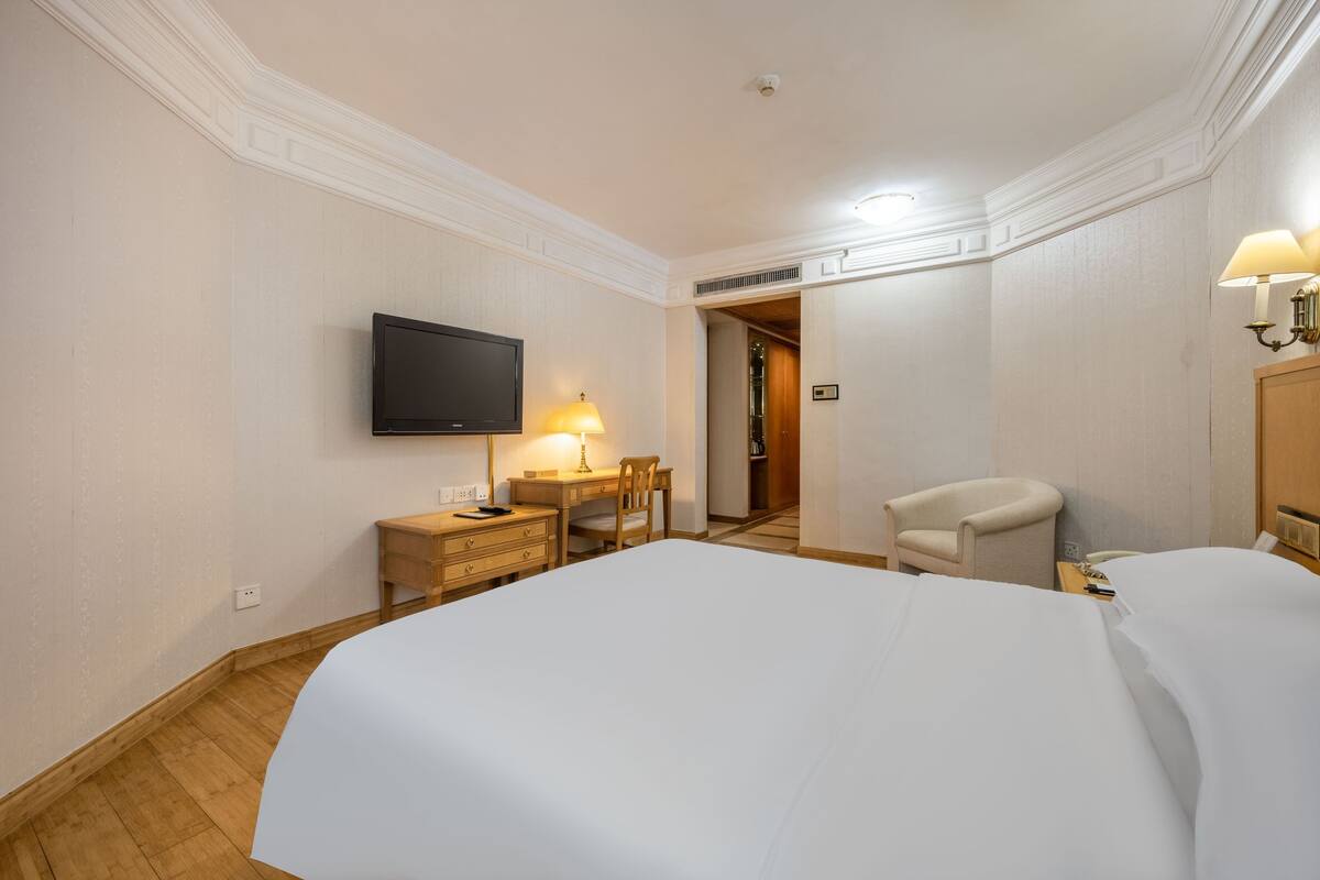 Una habitación de hotel con una cama grande, un escritorio con una lámpara, una silla, un televisor y una puerta que da a otra habitación.