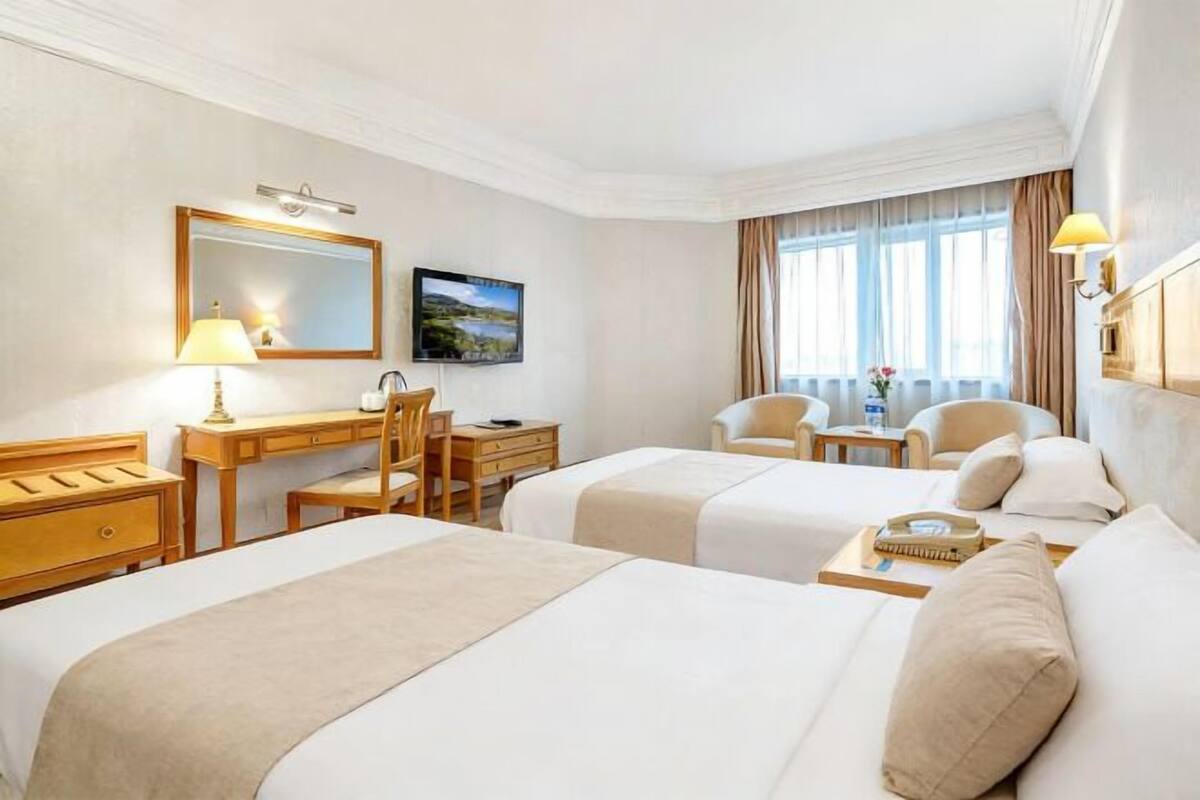 Habitación de hotel con dos camas, un escritorio, una silla, un televisor y una ventana con cortinas.