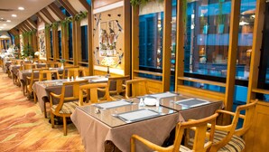 A hotel dining area with multiple tables and chairs, large windows, and a patterned carpet. - Hotel Silverland (Dongguan)