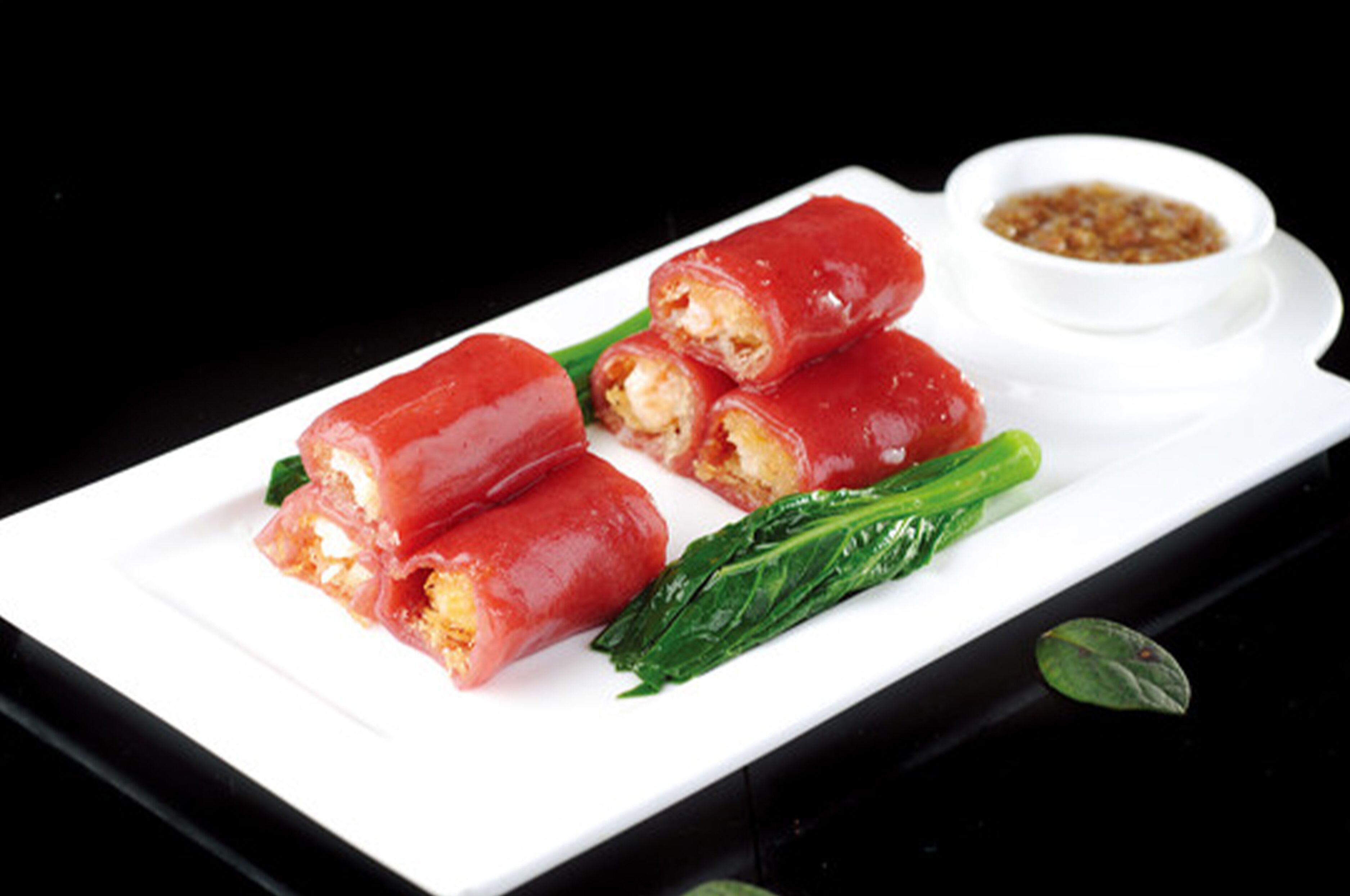 A plate with three red rolls and a small bowl of sauce.