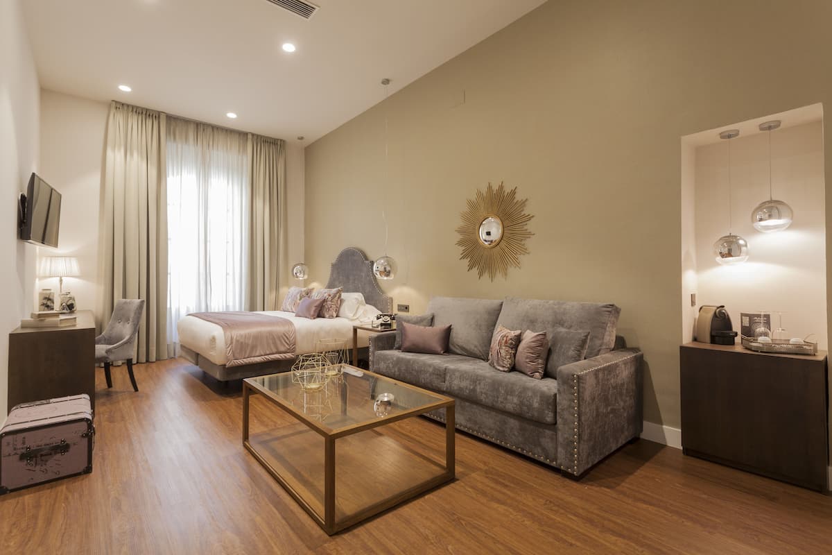 Une chambre d’hôtel comprenant un lit, un canapé, une table basse en verre, une télévision et un bureau avec une lampe.