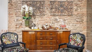 A room with two patterned armchairs, a wooden cabinet with drawers, and decorative wall art against a brick wall.