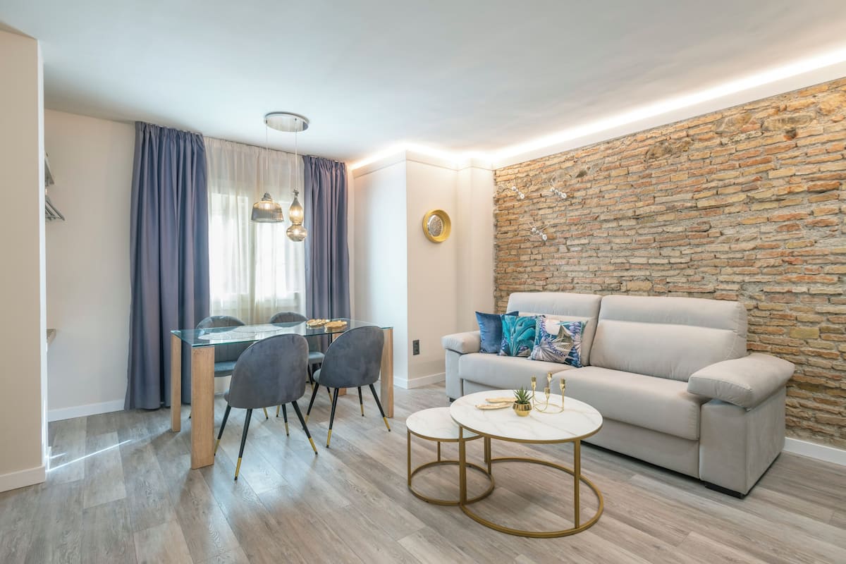 Un salon moderne avec un mur en pierre, un canapé beige, une table à manger en verre et une table basse ronde.