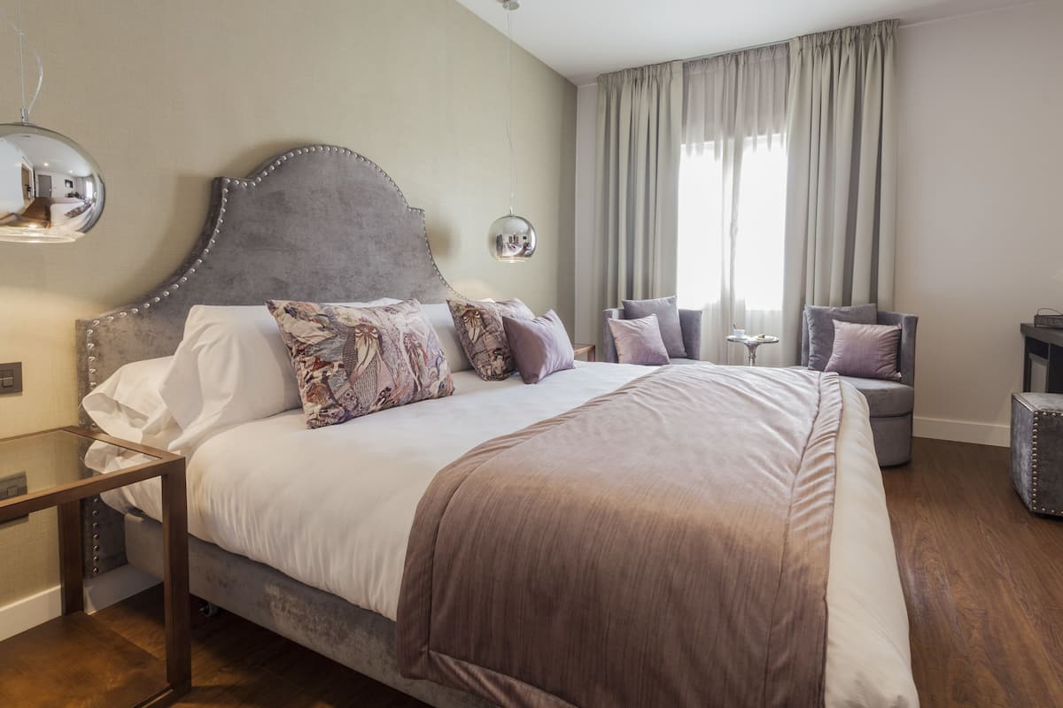 Une chambre à coucher bien rangée, avec un grand lit, une table de chevet, un miroir et une fenêtre avec des rideaux.