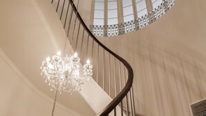 Una imponente escalera con candelabro, paredes curvas y amplios ventanales.