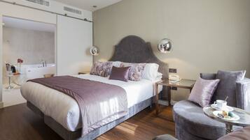 A modern hotel room with a large bed, bedside table, and a small round table with a cup and saucer.