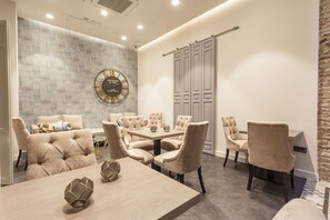 Una sala de conferencias moderna con una gran mesa redonda, sillas tapizadas en beige, un reloj de pared y un armario con puerta corredera.