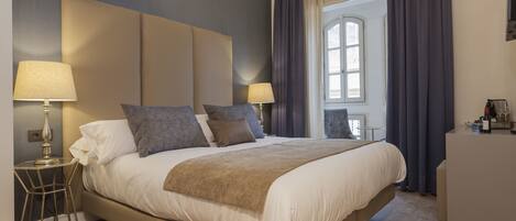 A modern bedroom with a large bed, two bedside tables with lamps, a dresser, and a window with curtains.