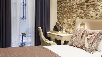 A hotel room with a bed, a desk, a chair, and a stone wall.