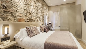 Un dormitorio moderno con pared de piedra, una cama grande con muchos cojines, un teléfono junto a la cama y una cabina de ducha de vidrio.