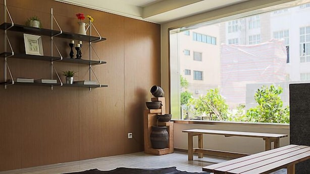 Ein modernes Wohnzimmer mit Holzregalen, einem schwarzen Lederteppich, einer hölzernen Bank und Blick auf Grünflächen.