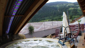 Un bain à remous avec vue sur un paysage montagneux. On y trouve des chaises longues et une table avec des parasols.