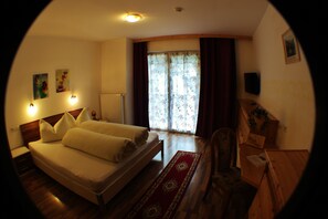 Une chambre à coucher avec un lit, un bureau en bois, une chaise, un radiateur et une fenêtre avec des rideaux.