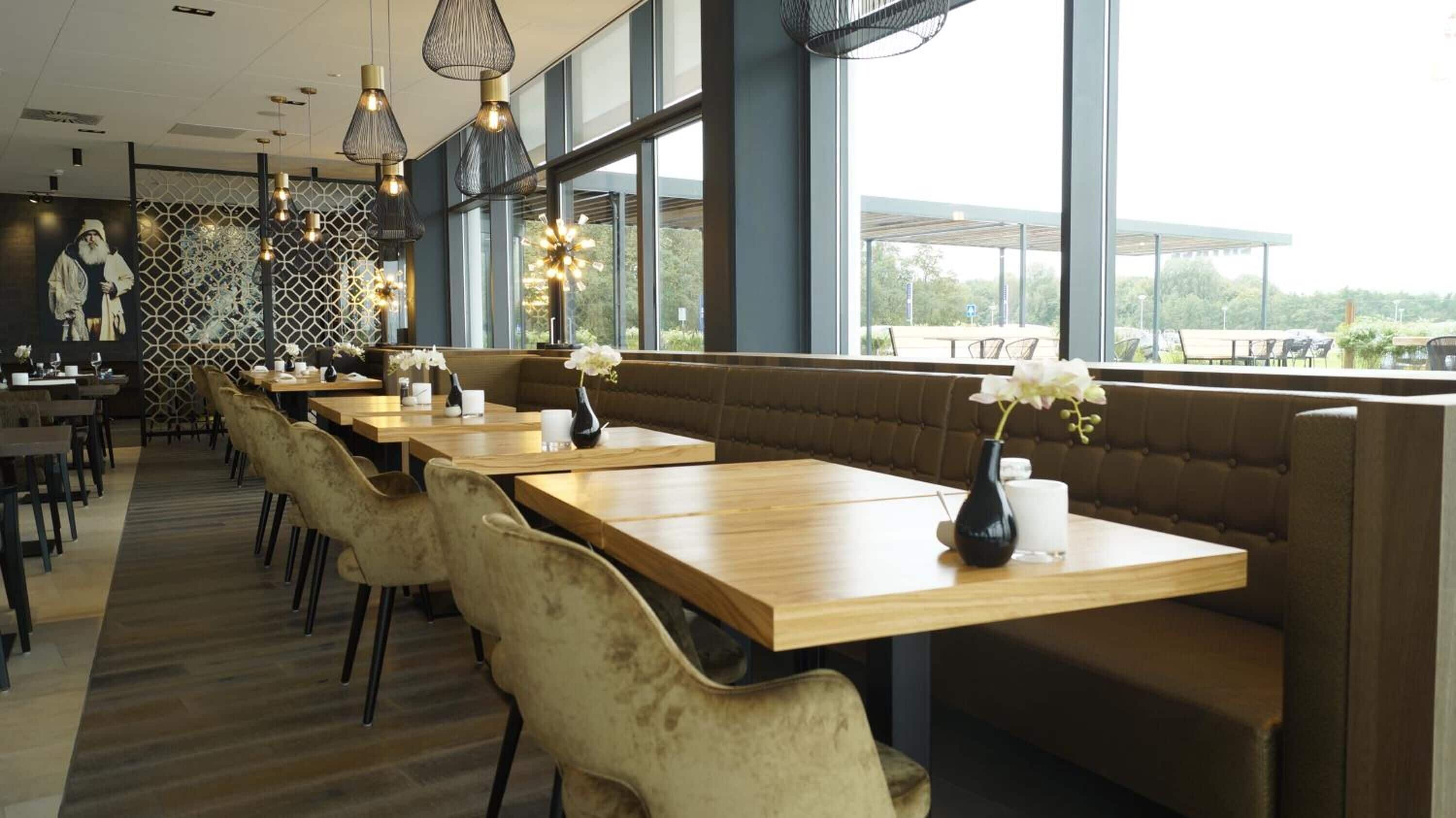 Un restaurante con largas mesas de madera, cabinas acolchadas, ventanas amplias y lámparas colgantes.
