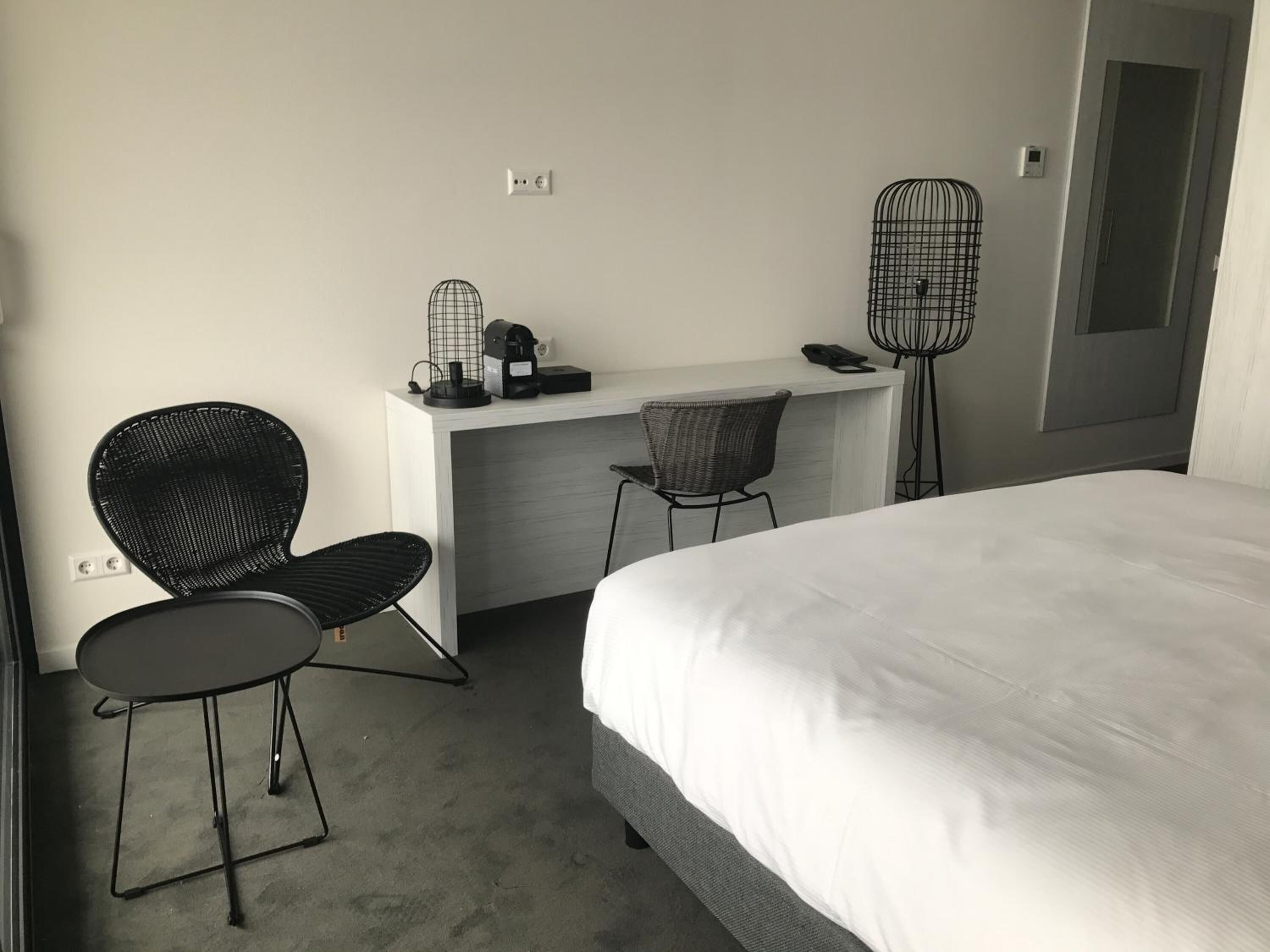 Una habitación de hotel con cama, escritorio, dos sillas y una mesita con cafetera.