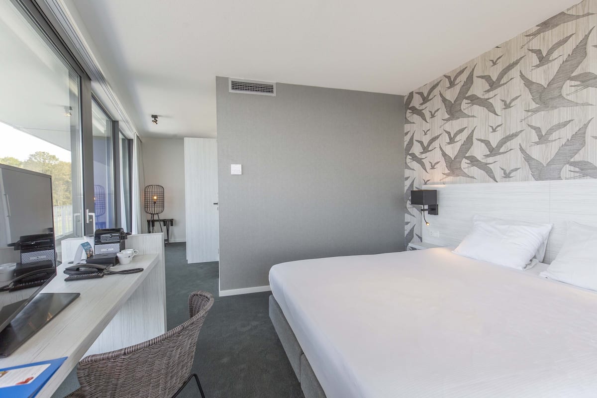 Ein Hotelzimmer mit einem Bett, einem Schreibtisch mit Computer, einem Stuhl und einem Fenster.