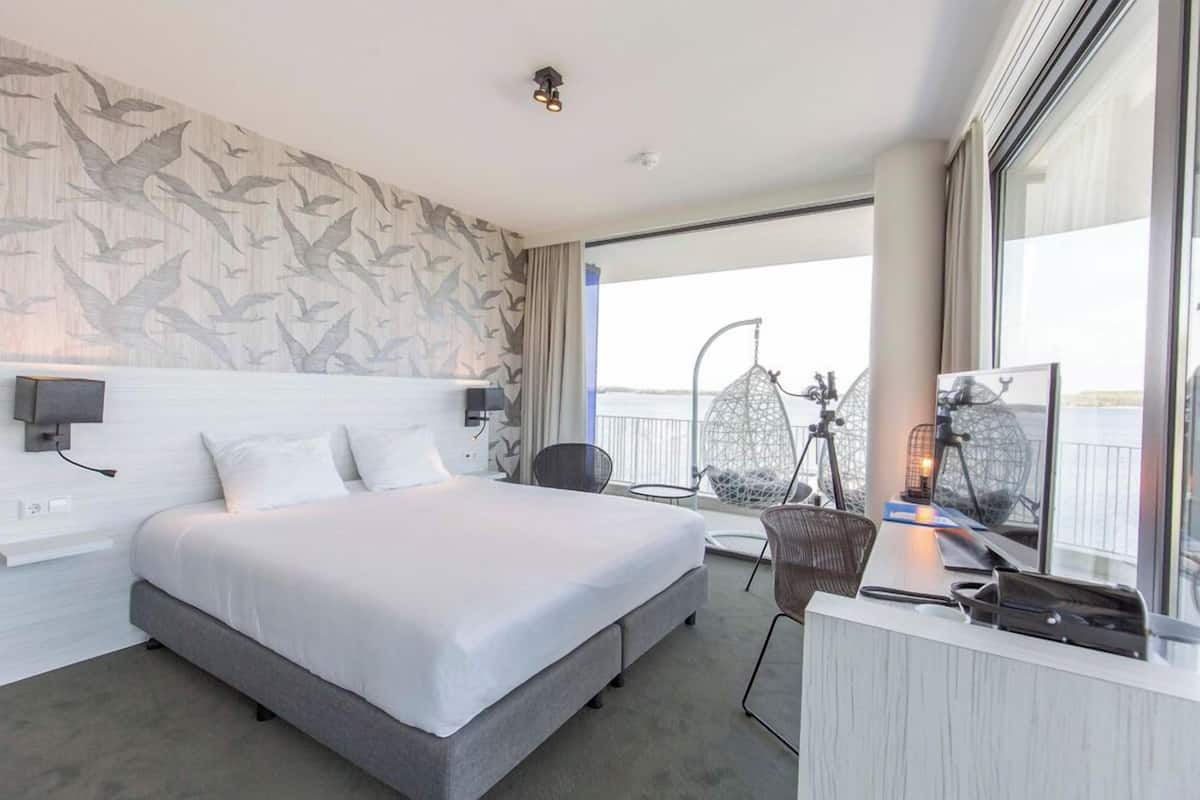 Ein modernes Hotelzimmer mit einem großen Bett, einem Schreibtisch, einem Sessel und einem Balkon mit Blick.