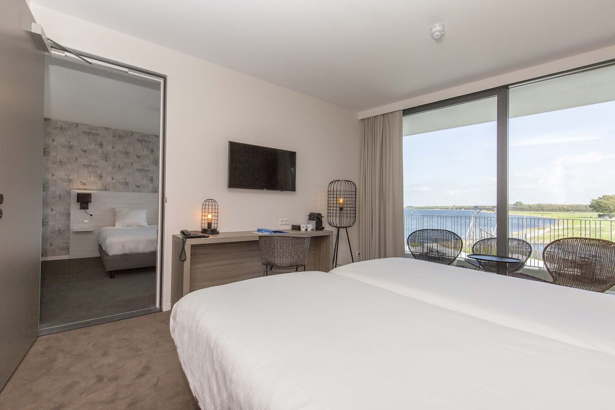 Ein Hotelzimmer mit Bett, Schreibtisch mit Stuhl, Fernseher und Balkon mit Sitzgelegenheiten.