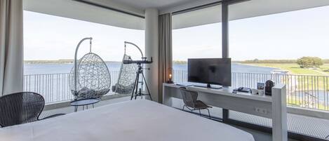 A hotel room with a large bed, a desk with a computer, two egg-shaped chairs, a telescope, and a TV.