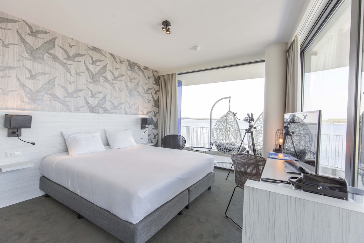 Ein modernes Hotelzimmer mit einem großen Bett, einem Schreibtisch und einem Balkon mit Blick.