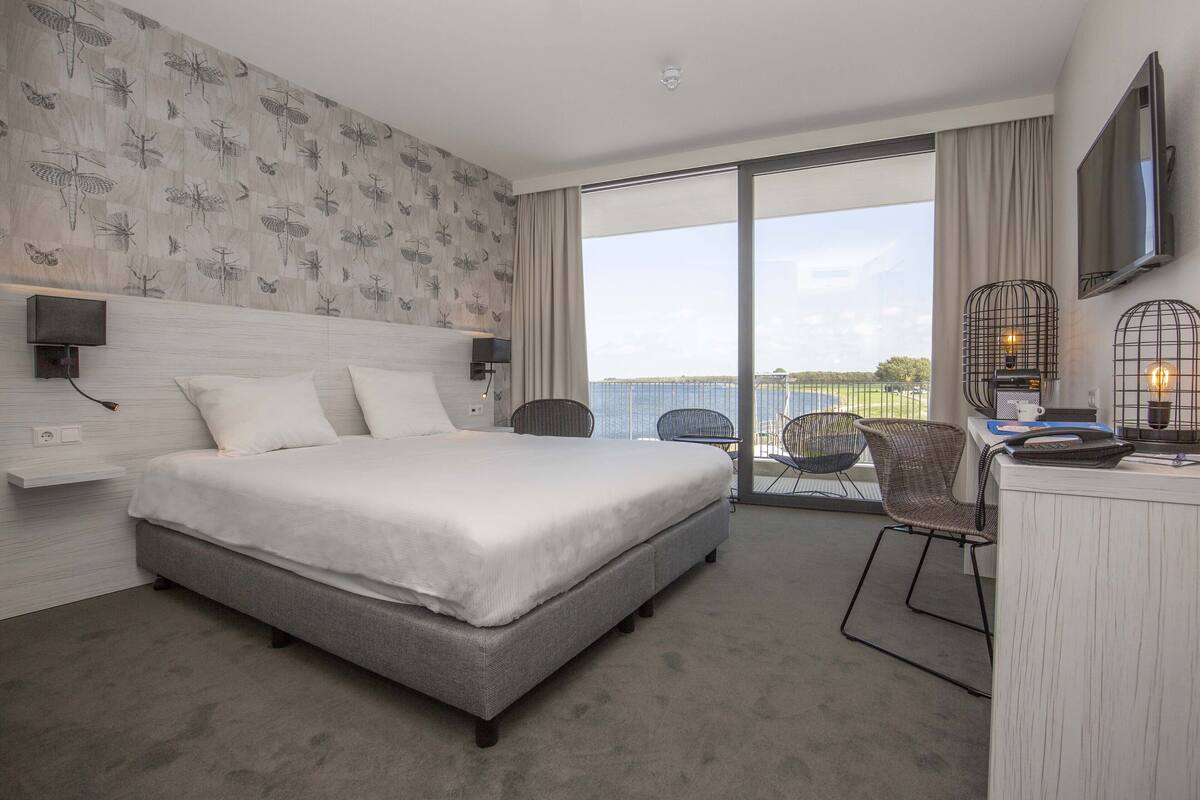 Ein modernes Hotelzimmer mit einem großen Bett, einem Schreibtisch mit Stuhl, einem Fernseher und einem Balkon mit Blick.