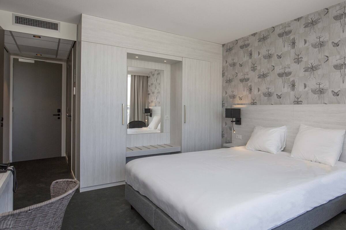 Ein modernes Hotelzimmer mit einem großen Bett, einem Nachttisch, einer Wandlampe und einer Wandtapete mit Muster.
