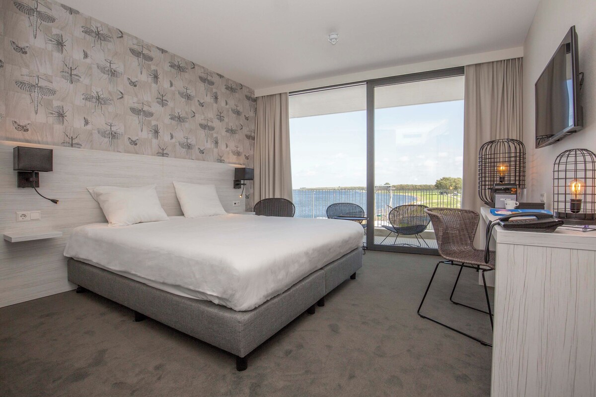 Ein modernes Hotelzimmer mit einem großen Bett, einem Schreibtisch mit Stuhl, einem Fernseher und einem Balkon mit Blick.