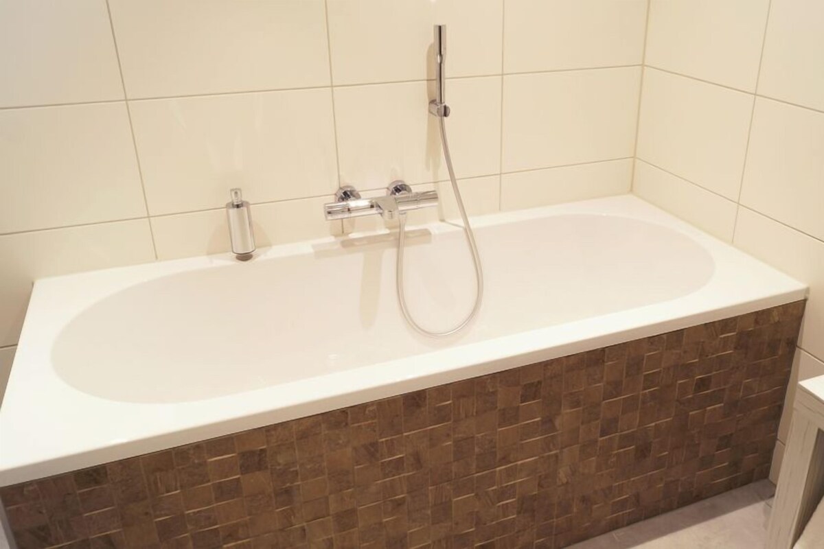 A bathroom with a bathtub, a shower, and a tiled wall.