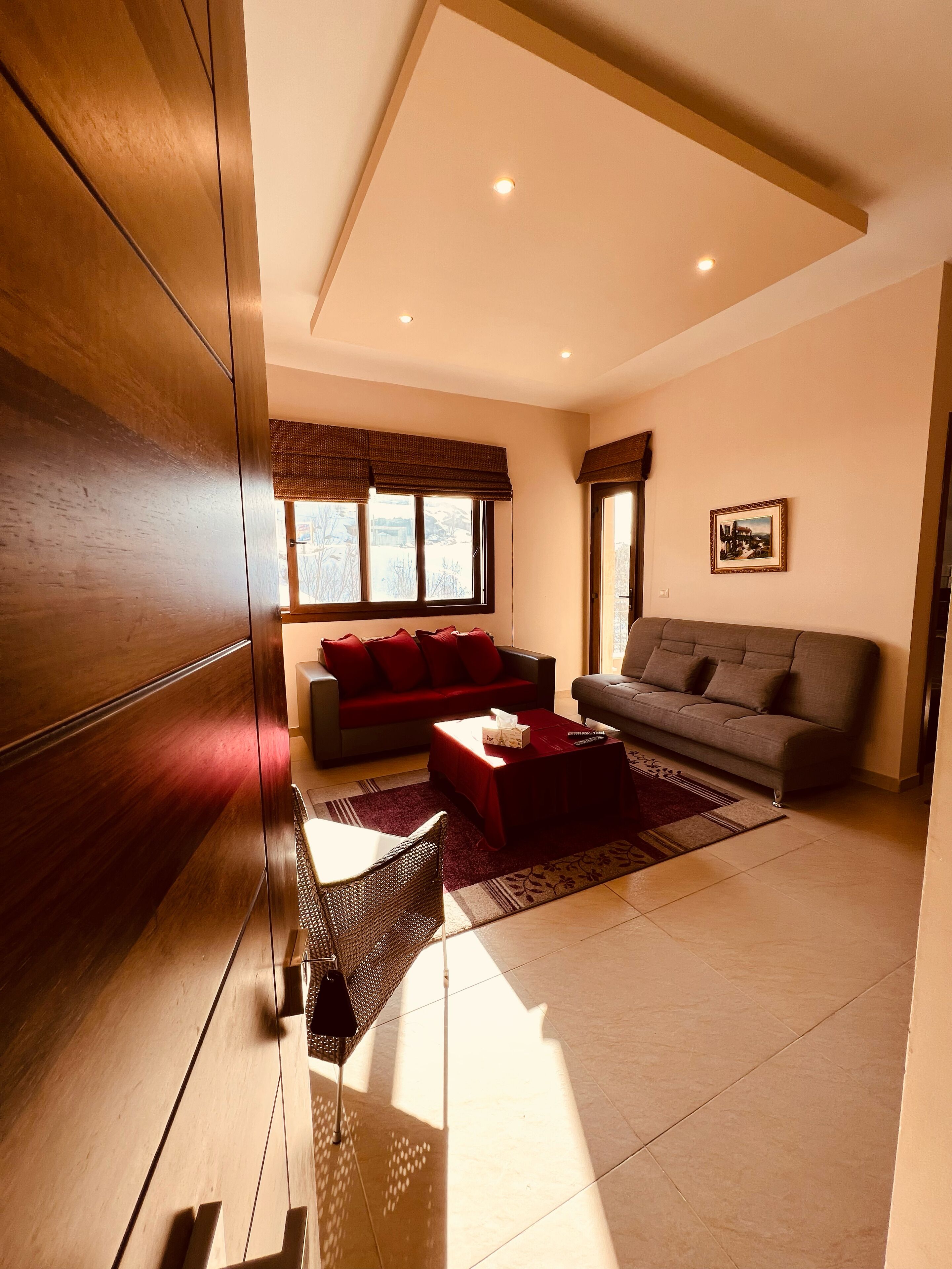 A modern living room with a wooden floor, two sofas, a coffee table, and a large window with blinds.