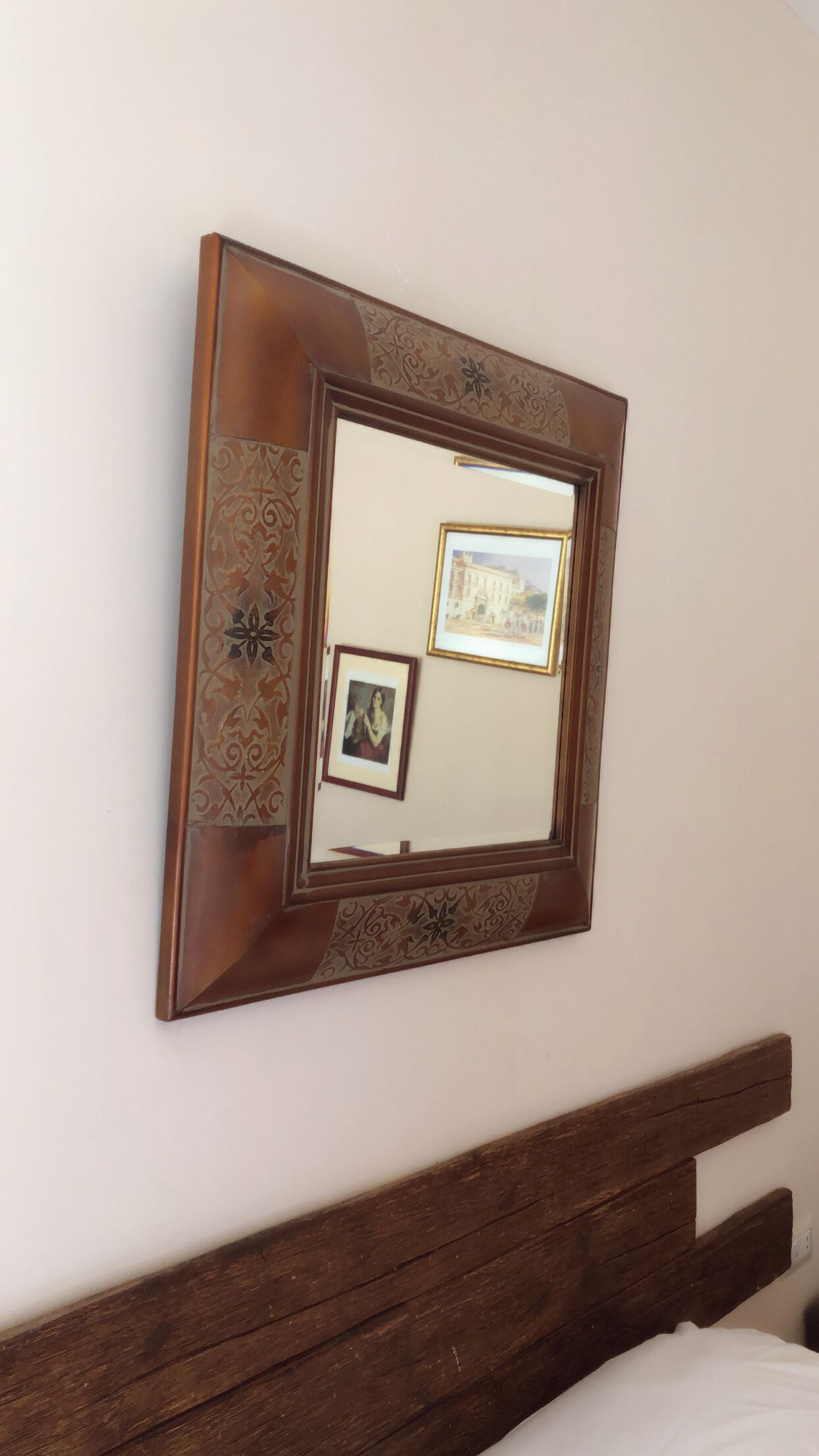 A wall-mounted mirror with decorative patterns and three framed pictures.