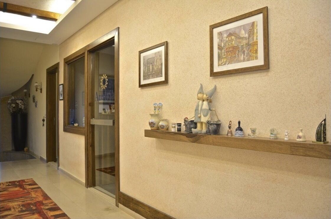 Un pasillo con un estante de madera que exhibe varios objetos decorativos, un cuadro enmarco de un edificio y una puerta de cristal que da a otra habitación.