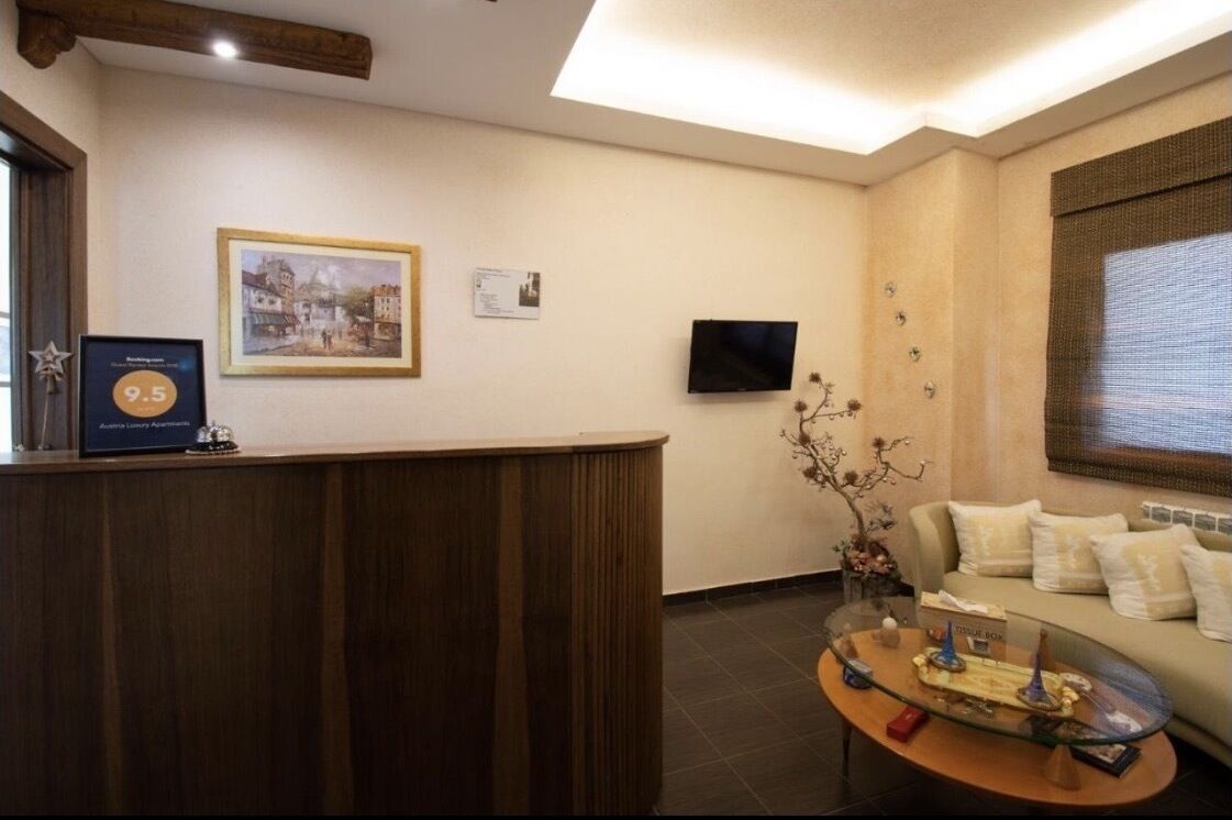 Un espace d’accueil comprenant un comptoir de réception en bois, un tableau encadré au mur, un téléviseur, un canapé avec des coussins et une table basse en verre agrémentée d’objets décoratifs.