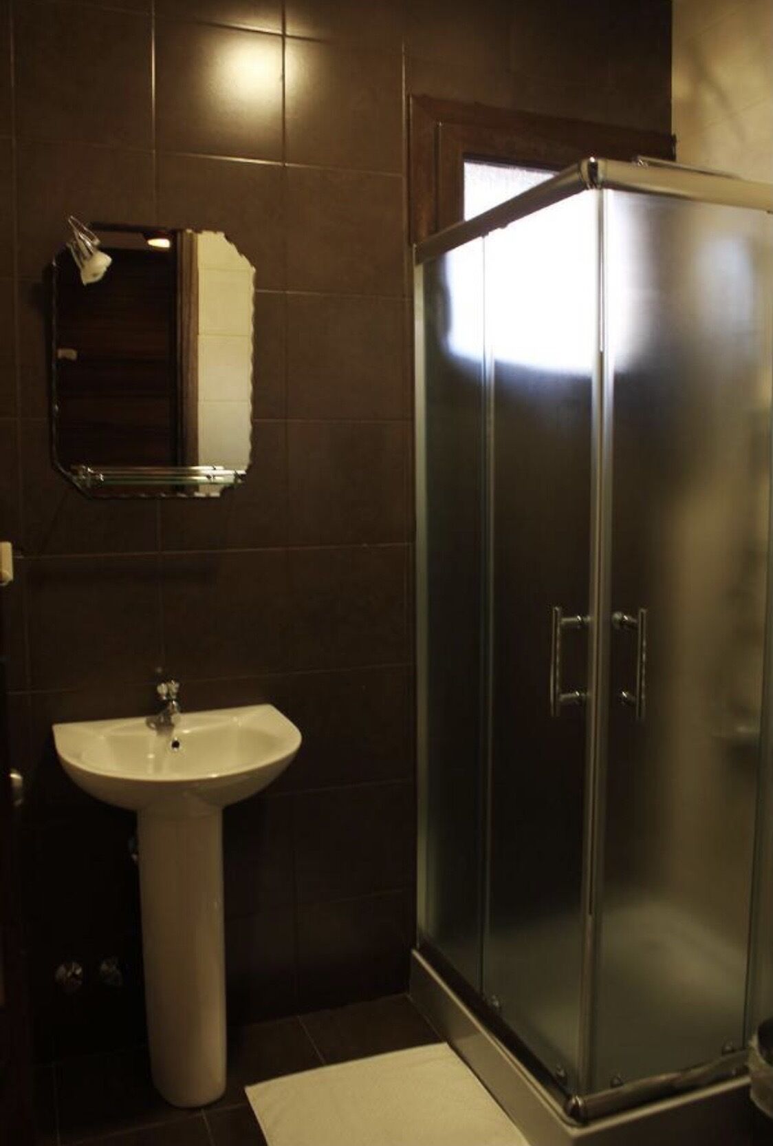 A bathroom with a white pedestal sink, a mirror, and a glass-enclosed shower.