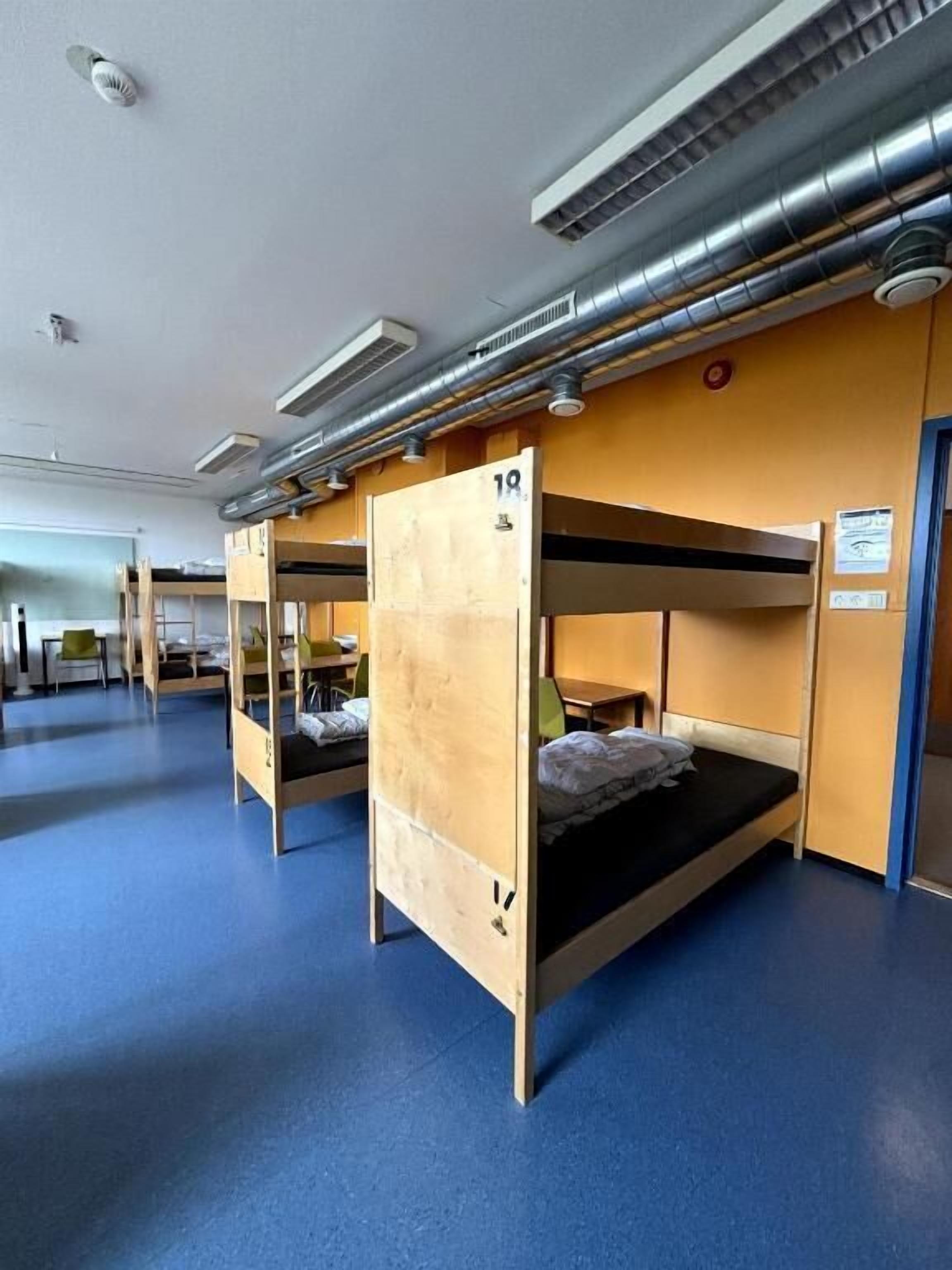 A dormitory room with bunk beds, numbered room 18, and a blue carpet.