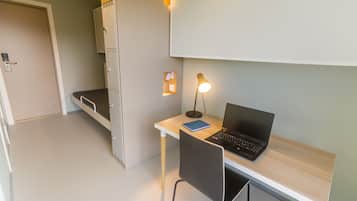 Una habitación moderna con escritorio, dos portátiles, una silla, una lámpara y un ventanal pequeño.