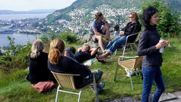 A group of people sitting on chairs on a grassy hill overlooking a town and a body of water.
