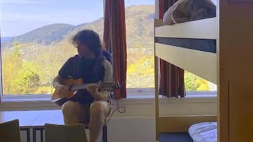 A room with bunk beds, a window with curtains, a chair, and a guitar.