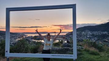 Una persona de pie frente a una vista enmarcada de un atardecer sobre un paisaje urbano.