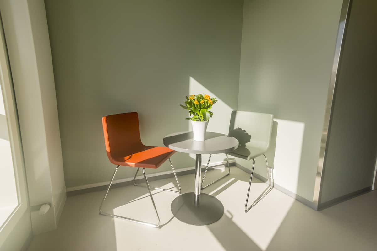Ein modernes Zimmer mit einem runden Tisch, einem einzelnen orangefarbenen Sessel und einer Topfpflanze.