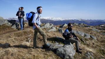 A group of hikers on a rocky mountain trail with snow-capped peaks in the background.