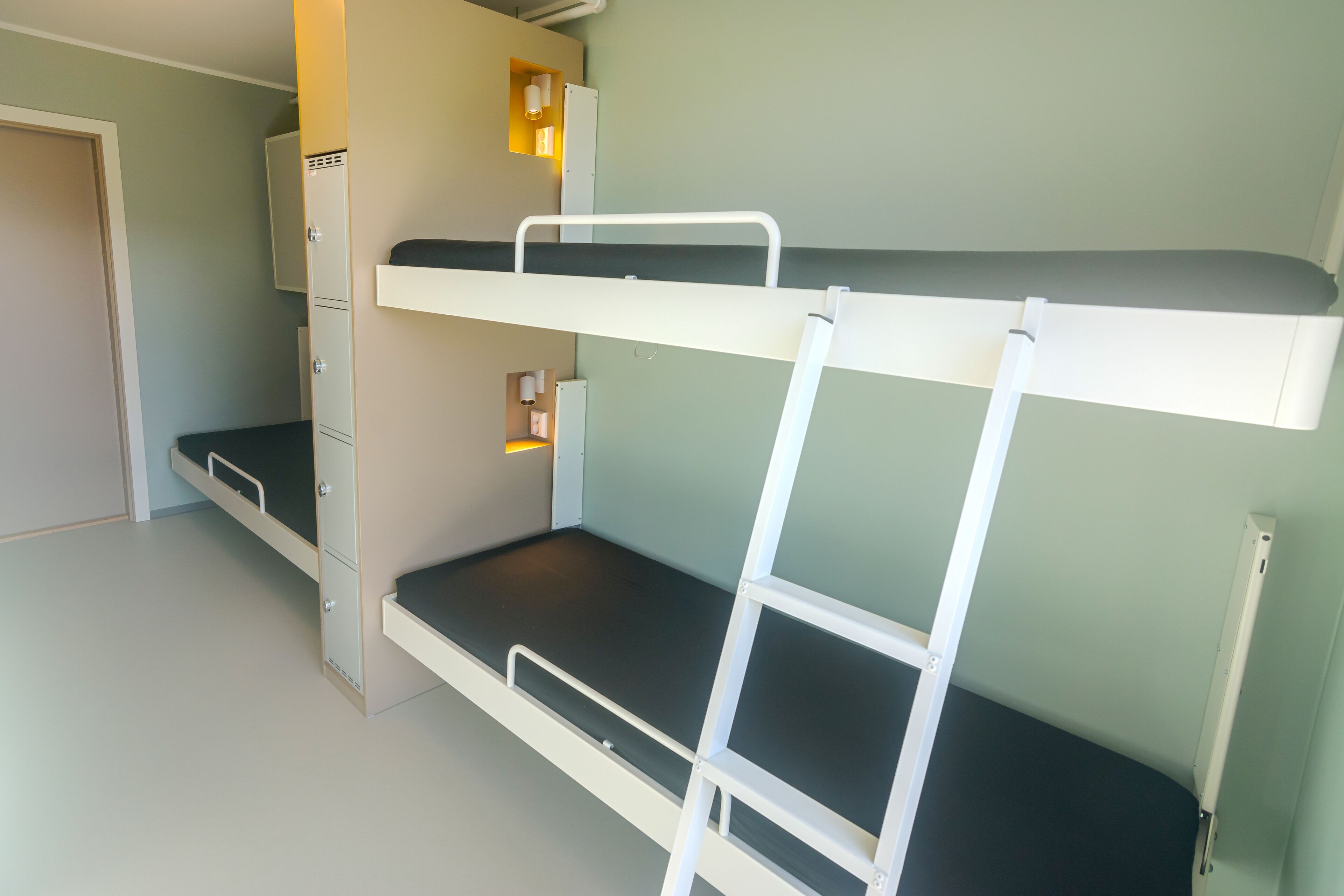 A bunk bed with a ladder, a desk, and a cabinet in a room with light green walls.