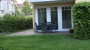 A patio area with a table and chairs, surrounded by greenery and a building with a balcony. - Ferienoase Usedom (Heringsdorf)
